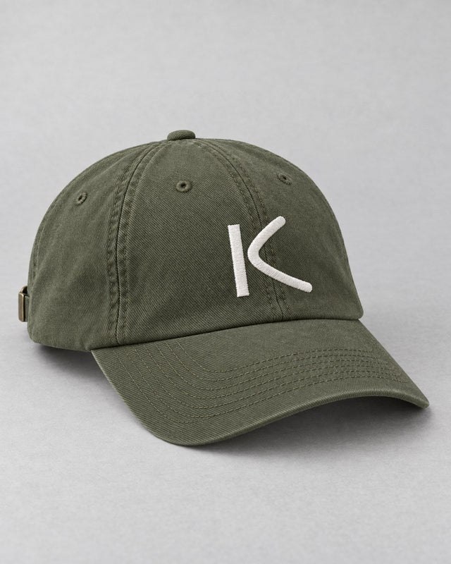 An olive six-panel cap with a chalk-white K stitched on the front.
