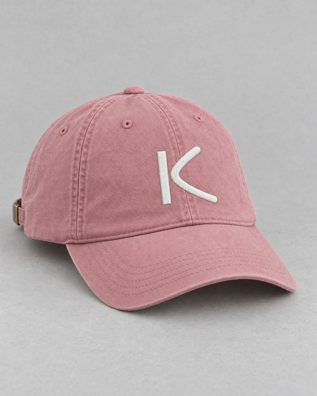 A dusty-pink six-panel cap with a chalk-white K stitched on the front.