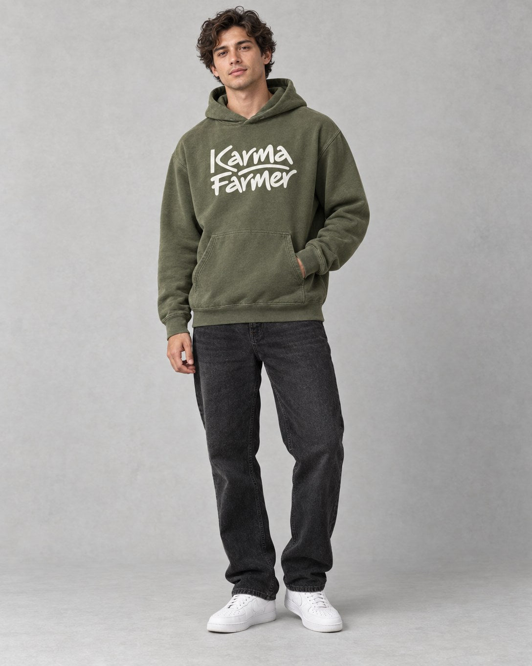 A person wearing the olive Signature Hoodie with washed black jeans against a grey backdrop.