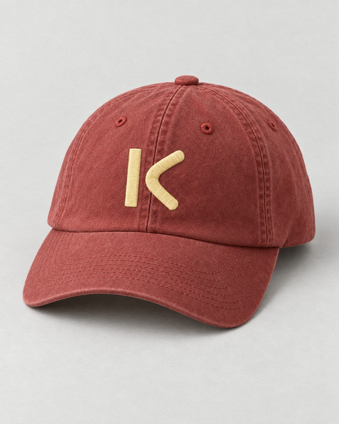 A washed brick-red cap with a pale yellow K stitched on the front.