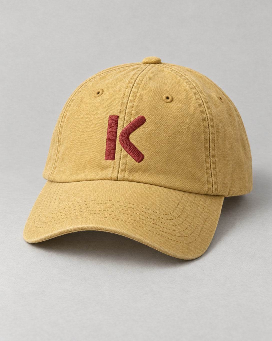 A faded yellow cap with a brick-red K stitched on the front.