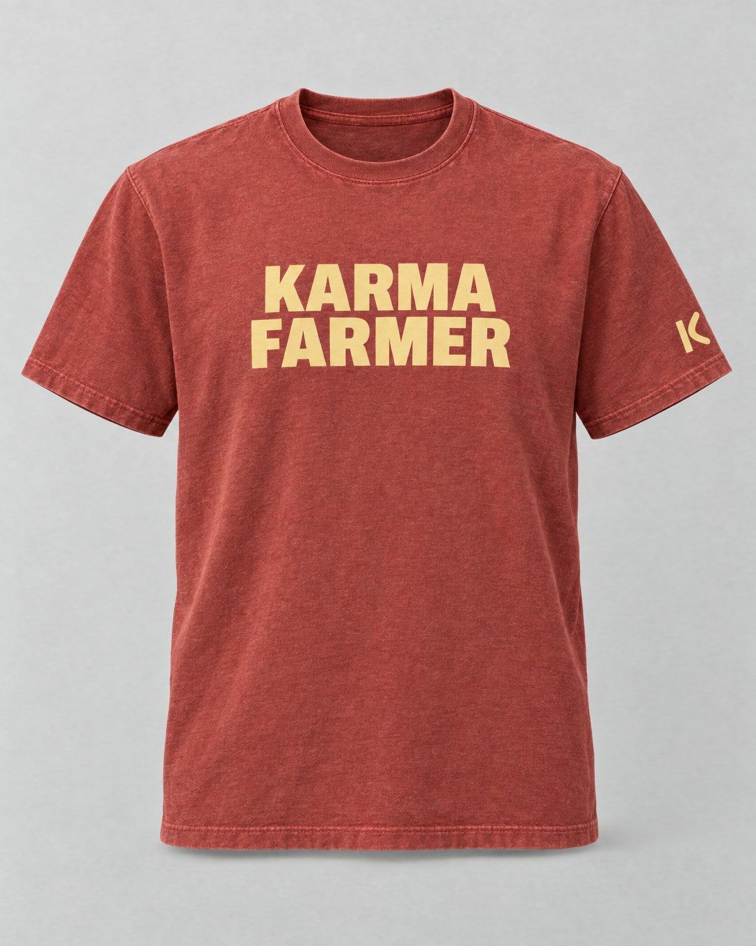The sun-faded red Summer Tee from the front, with KARMA FARMER in pale yellow block capitals and a small K on the sleeve.